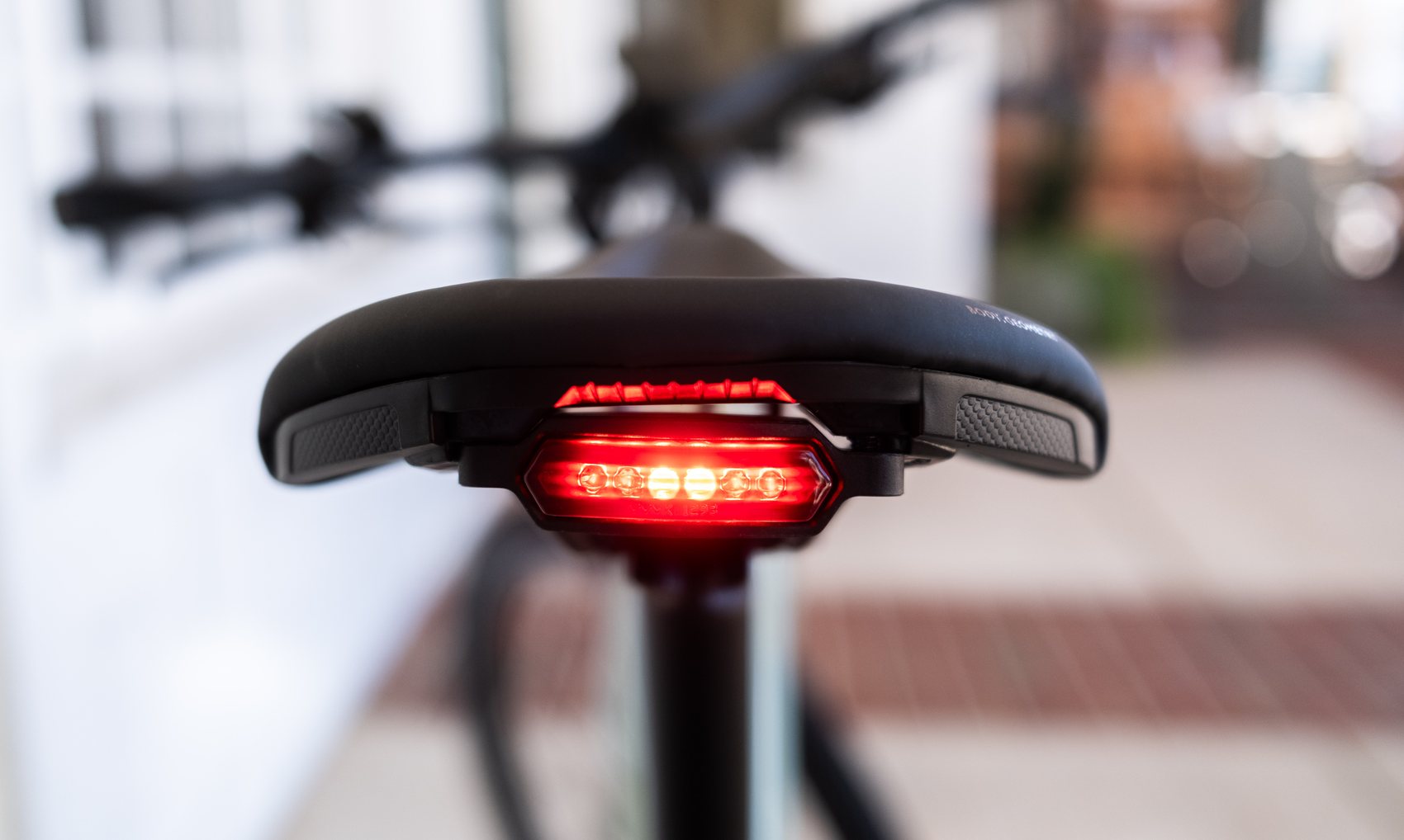 Close-up of the back of a black saddle with a lit red LED tail light built into it